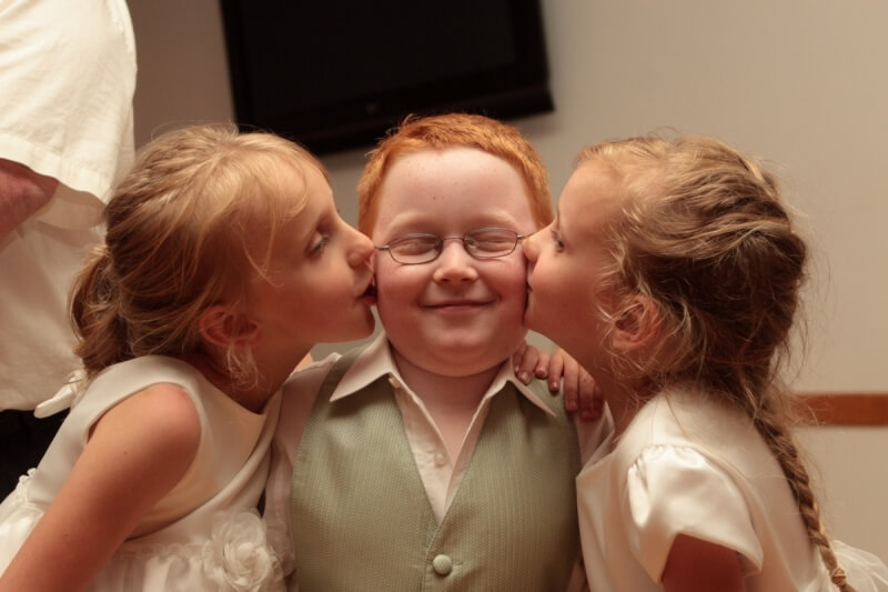 Three young children kissing at a wedding